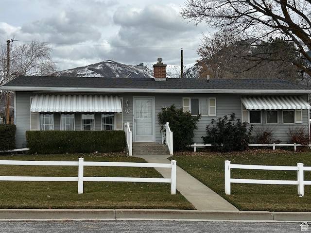 ranch-style home featuring a fenced front yard, a chimney, a front yard, and roof with shingles