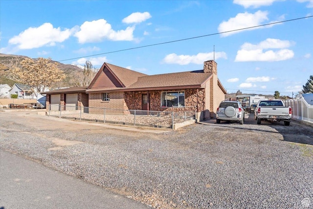 ranch-style house with driveway, stone siding, a chimney, a fenced front yard, and a mountain view