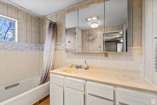 full bath featuring shower / bath combo with shower curtain, vanity, tile walls, and decorative backsplash
