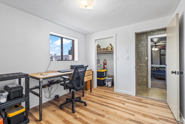 office area with baseboards, light wood-style flooring, and a textured ceiling