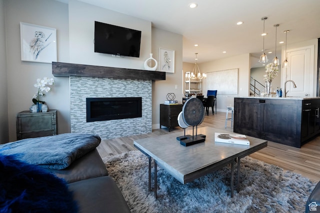 living area featuring light wood-type flooring, a glass covered fireplace, recessed lighting, baseboards, and a chandelier