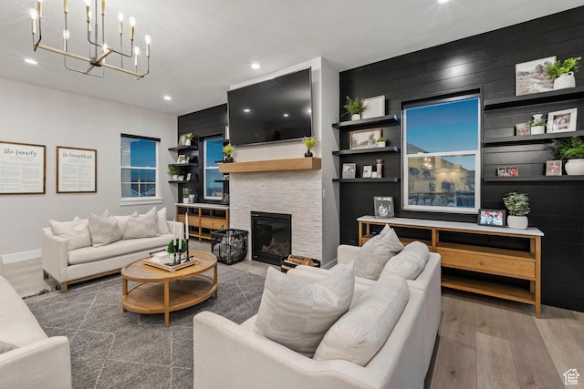 living room with recessed lighting, a notable chandelier, a stone fireplace, and wood finished floors