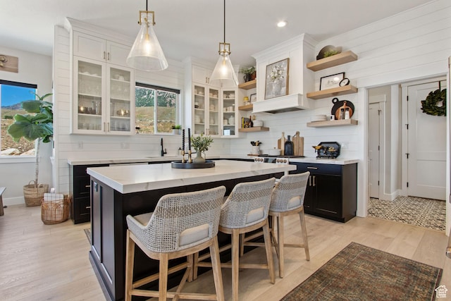 kitchen with decorative backsplash, light wood finished floors, a breakfast bar, open shelves, and dark cabinetry