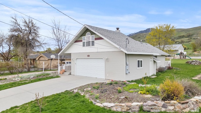 view of property exterior featuring a chimney, roof with shingles, a lawn, a mountain view, and concrete driveway
