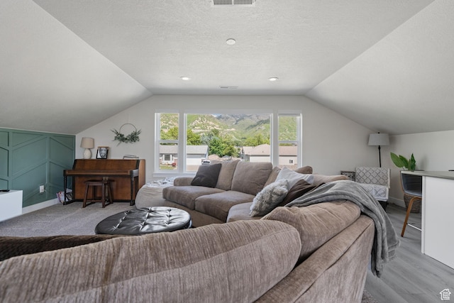 living room featuring lofted ceiling, visible vents, light wood-style floors, and a textured ceiling