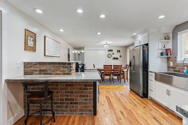 kitchen with stainless steel refrigerator with ice dispenser, light wood-type flooring, a sink, white cabinets, and light stone countertops
