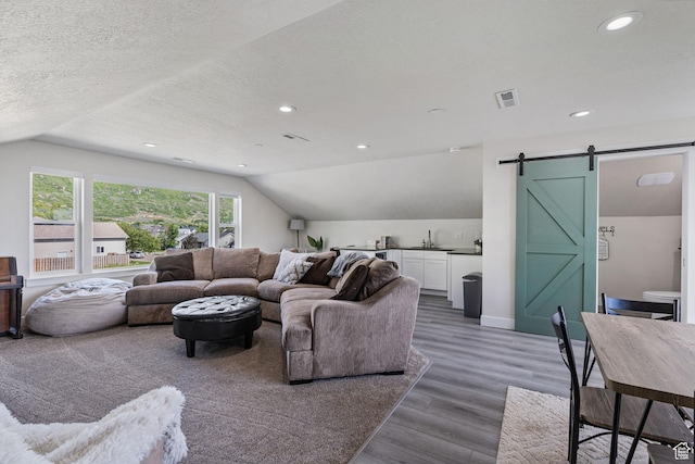 living area featuring a barn door, wood finished floors, a textured ceiling, lofted ceiling, and visible vents