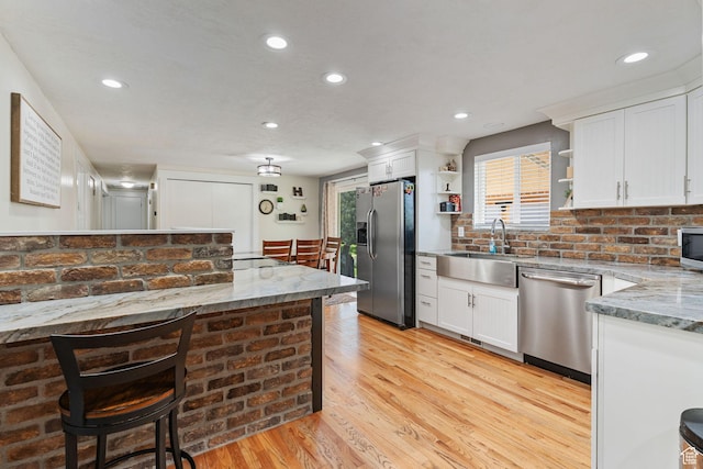 kitchen with a sink, open shelves, light wood finished floors, white cabinetry, and appliances with stainless steel finishes