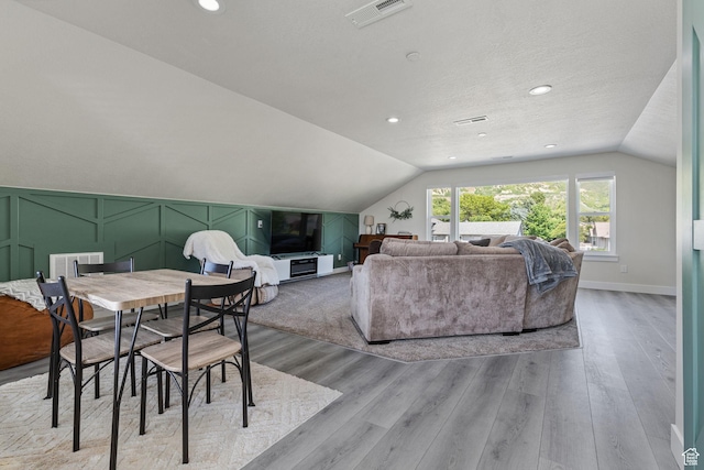 dining space featuring light wood-style floors, a textured ceiling, lofted ceiling, and visible vents