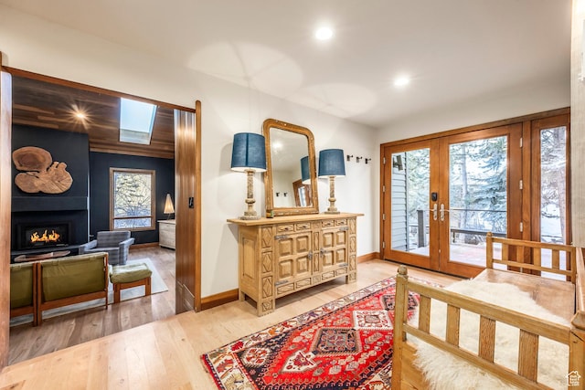 entryway with light wood-style flooring, baseboards, recessed lighting, a lit fireplace, and french doors