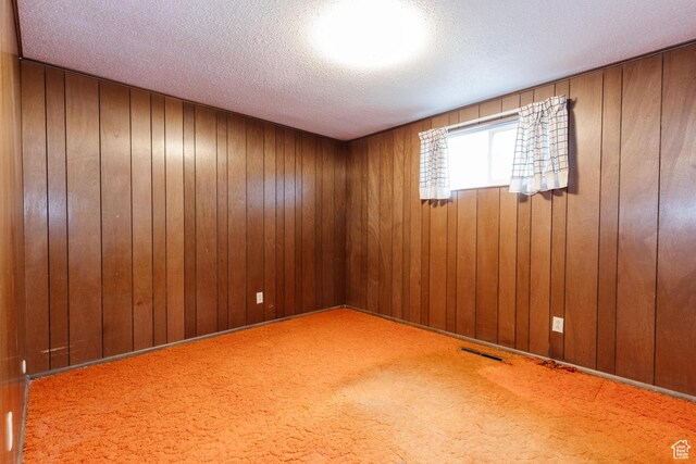 carpeted empty room featuring visible vents, a textured ceiling, and wood walls