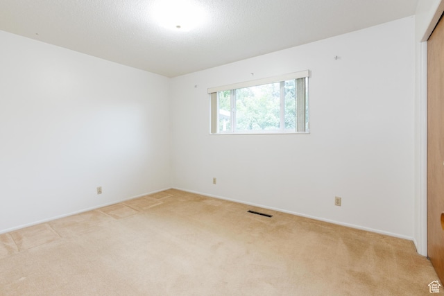unfurnished room with a textured ceiling, baseboards, light colored carpet, and visible vents