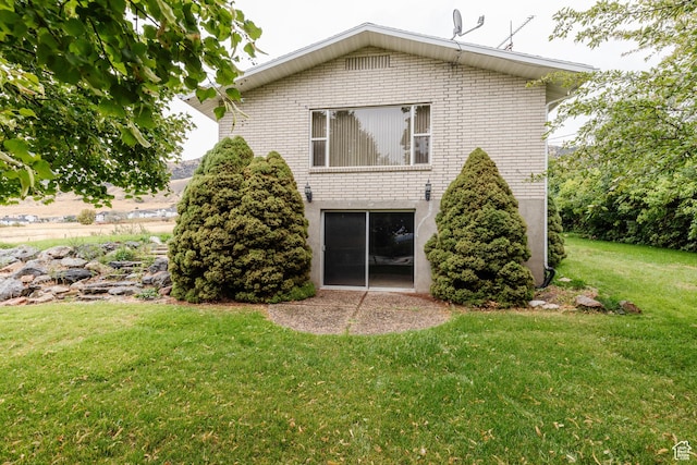 back of property featuring a lawn and brick siding