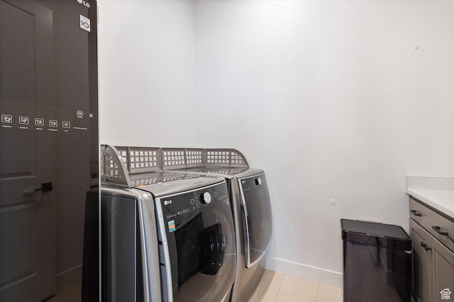 washroom featuring light tile patterned flooring, washer and clothes dryer, cabinet space, and baseboards