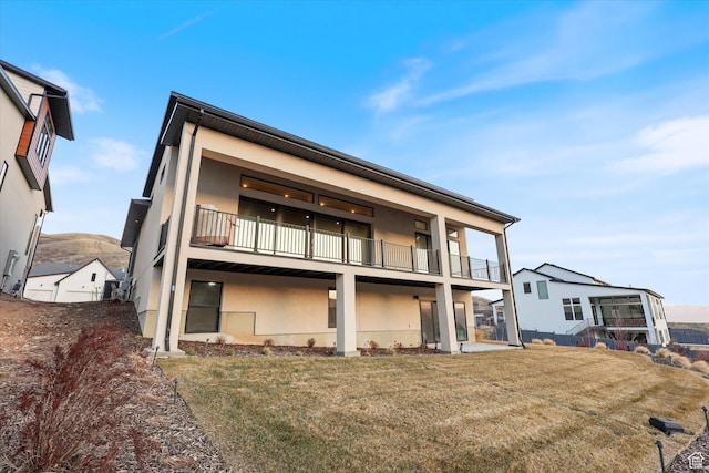 back of house with a balcony, stucco siding, and a yard