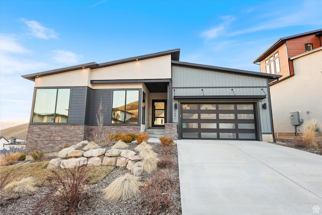 contemporary home with stone siding, a garage, and concrete driveway