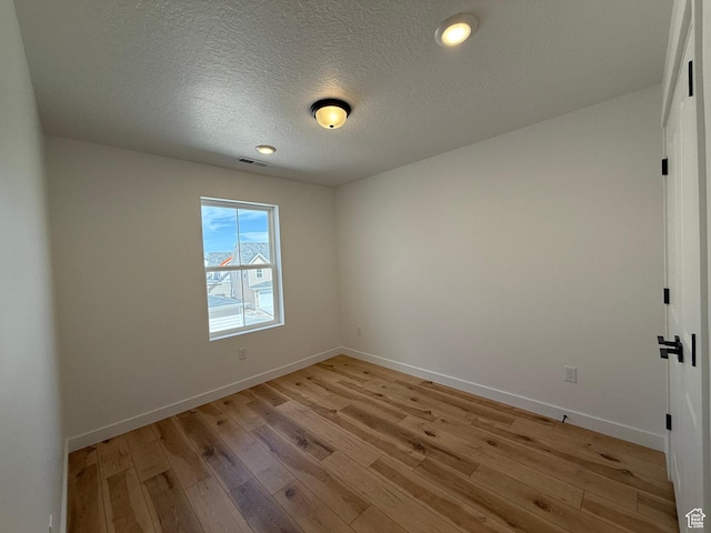 empty room featuring visible vents, baseboards, light wood-type flooring, and a textured ceiling