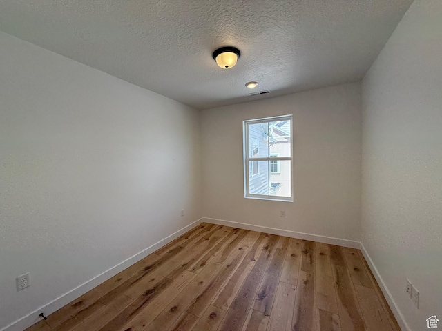 unfurnished room with light wood finished floors, visible vents, baseboards, and a textured ceiling