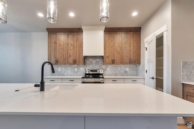 3240 W Oxford Loop Unit 219, Mountain Green, UT 84050 - kitchen featuring stainless steel range with electric stovetop, light countertops, tasteful backsplash, a sink, and brown cabinetry