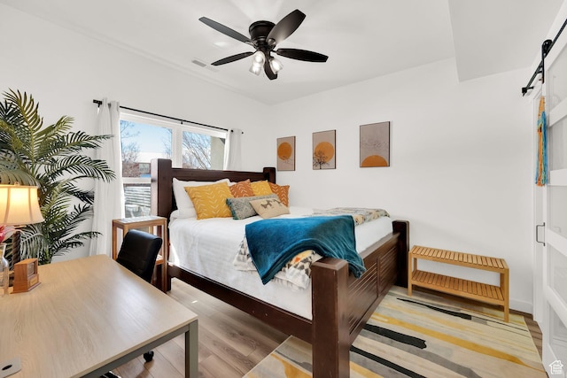 bedroom featuring visible vents, ceiling fan, light wood-type flooring, and a barn door