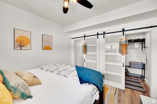 bedroom featuring a barn door, baseboards, a ceiling fan, and wood finished floors