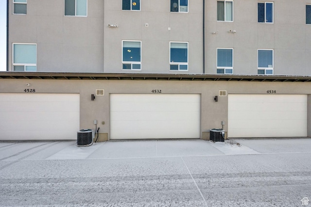 exterior space with an attached garage, central air condition unit, and stucco siding