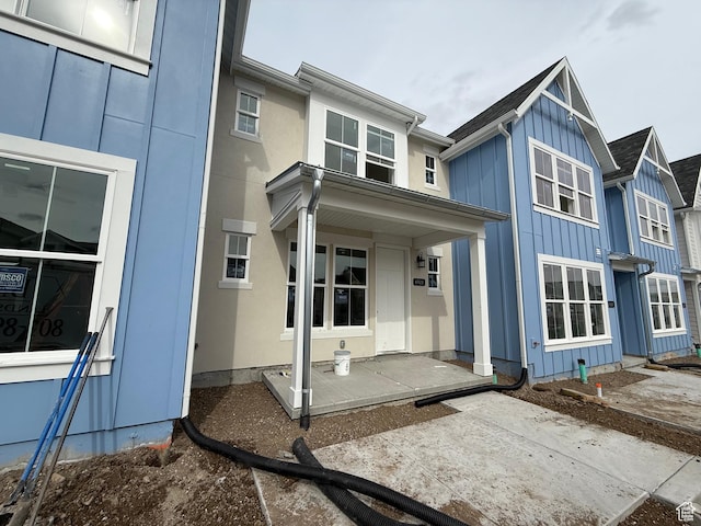 rear view of house with stucco siding, covered porch, and board and batten siding