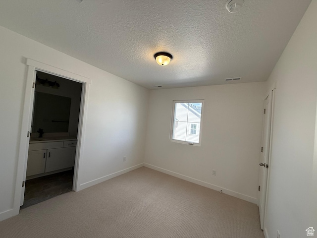 unfurnished bedroom with a textured ceiling, light colored carpet, baseboards, and visible vents