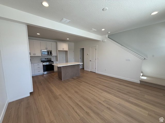 kitchen featuring open floor plan, light wood-type flooring, white cabinets, and stainless steel appliances