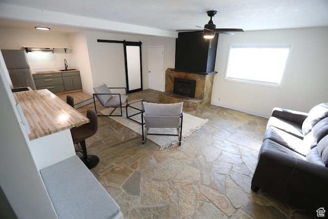 living room featuring stone tile flooring, baseboards, a barn door, and ceiling fan
