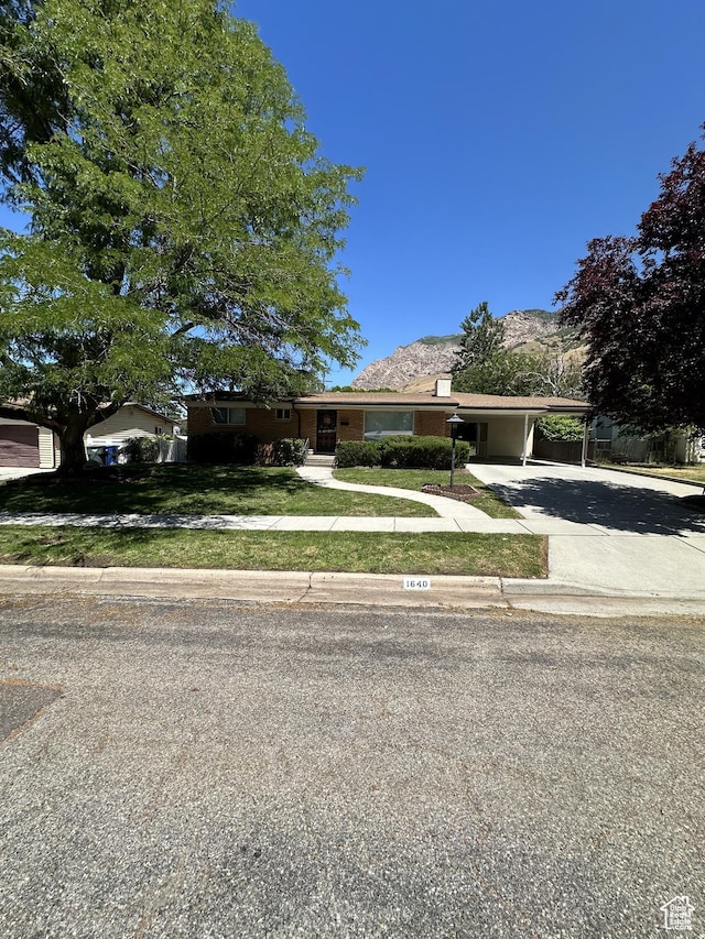 view of front of home with an attached carport, driveway, a mountain view, and a front lawn