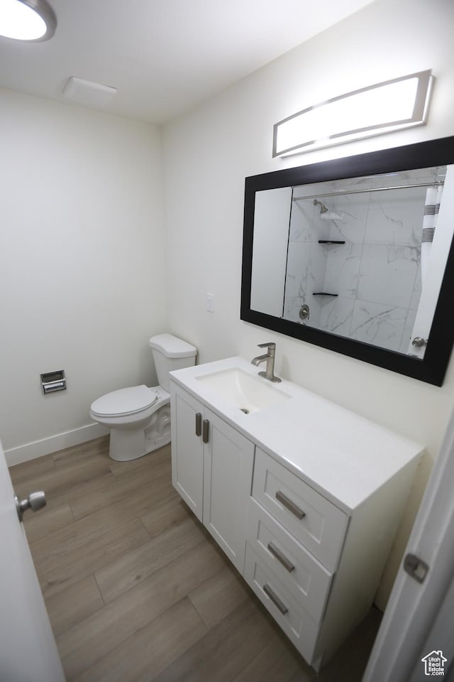 full bath featuring a shower, vanity, toilet, baseboards, and wood finished floors