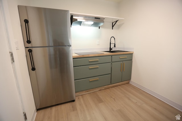 kitchen featuring green cabinets, black electric cooktop, light wood-style floors, exhaust hood, and freestanding refrigerator