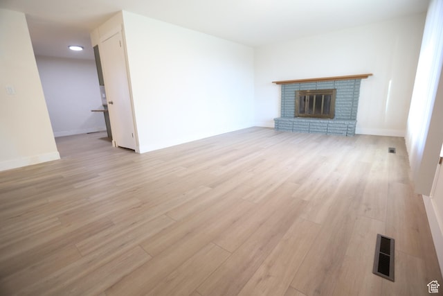 unfurnished living room with baseboards, a fireplace, visible vents, and light wood-style floors
