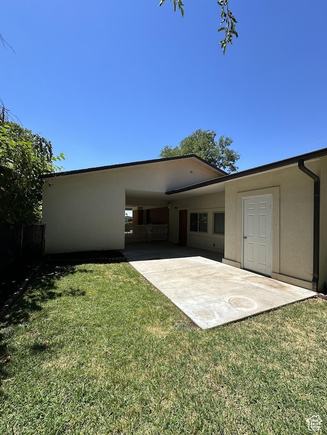 rear view of house with a lawn, fence, and stucco siding