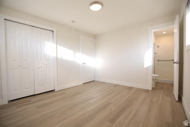 unfurnished bedroom featuring connected bathroom, baseboards, and light wood-style flooring