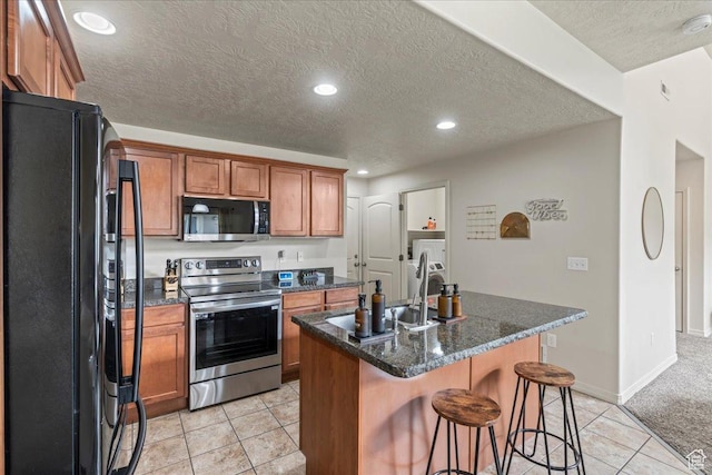 576 E 1540 S, Lehi, UT 84043 - kitchen with washer and clothes dryer, a breakfast bar area, brown cabinetry, stainless steel appliances, and a kitchen island with sink