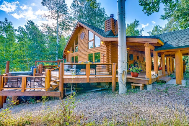 rear view of property with log siding, a shingled roof, a chimney, and a deck