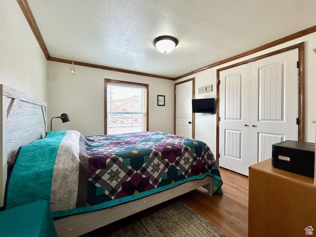 bedroom with a closet, a textured ceiling, wood finished floors, and crown molding