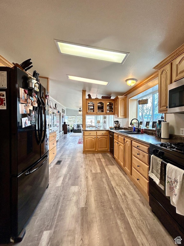 kitchen with light wood-style flooring, dark countertops, glass insert cabinets, a sink, and black appliances