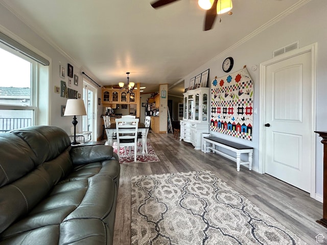 living room with ceiling fan with notable chandelier, visible vents, wood finished floors, and ornamental molding