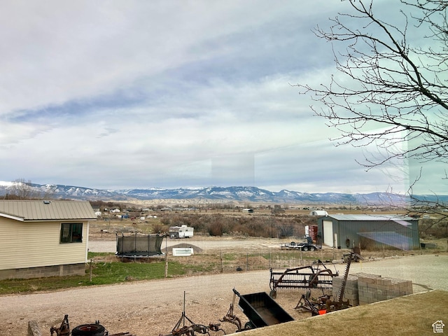 view of yard featuring a storage unit, an outdoor structure, a mountain view, and a trampoline