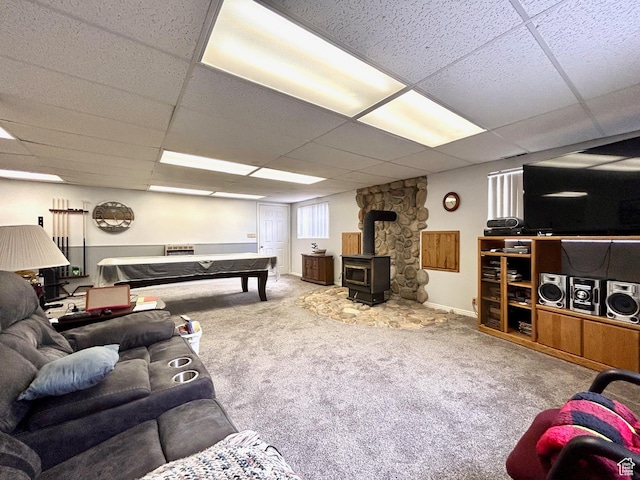 living room with baseboards, a wood stove, carpet, and a drop ceiling