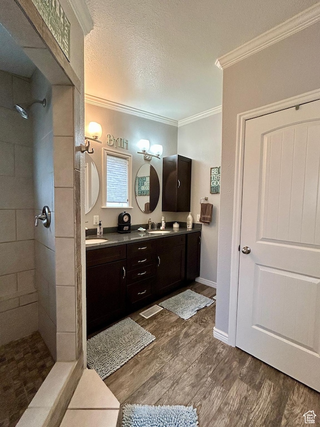 full bath with crown molding, double vanity, wood finished floors, and tiled shower