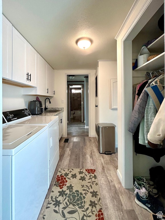 laundry area featuring a sink, light wood finished floors, a textured ceiling, independent washer and dryer, and cabinet space