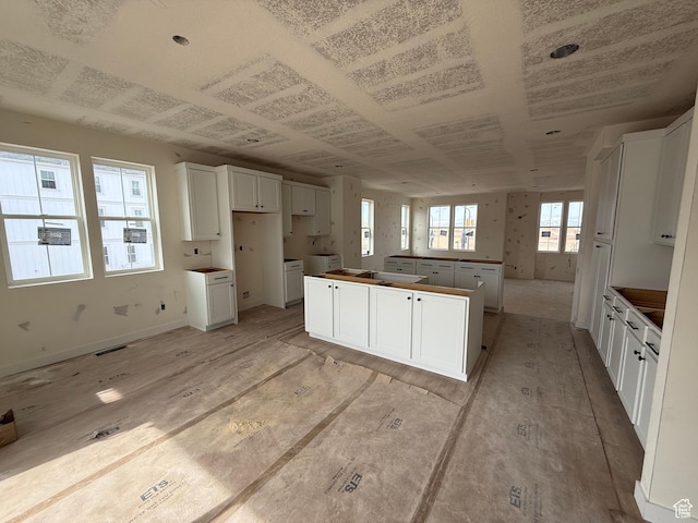 kitchen with baseboards, white cabinets, visible vents, and a center island