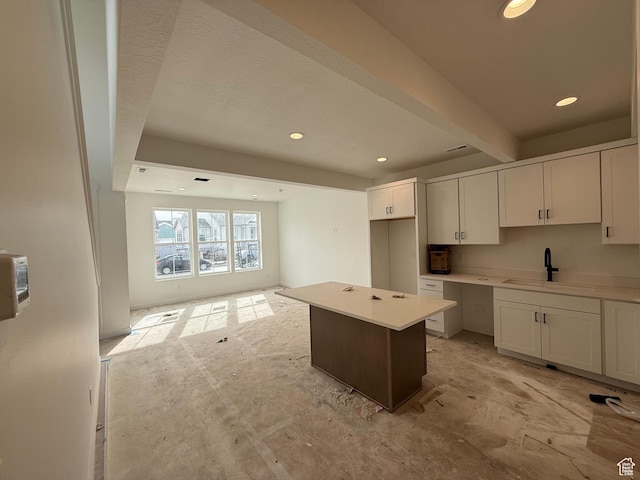 kitchen with beam ceiling, a sink, a center island, white cabinets, and recessed lighting