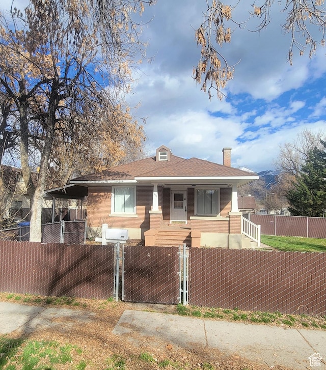 view of front of house with a gate, covered porch, a chimney, brick siding, and a fenced front yard