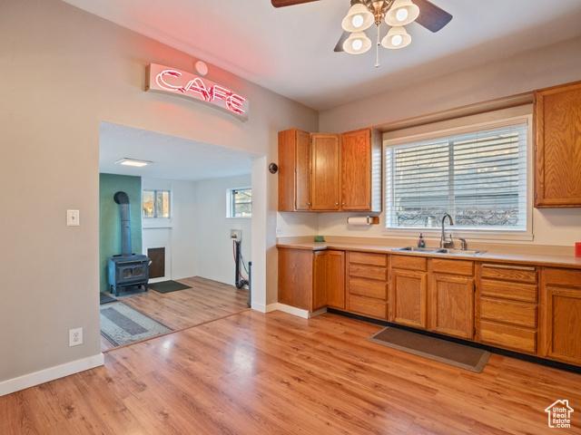 kitchen with light countertops, light wood-style flooring, a ceiling fan, a sink, and a wood stove