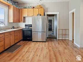 kitchen featuring light countertops, stove, a sink, light wood-style floors, and freestanding refrigerator